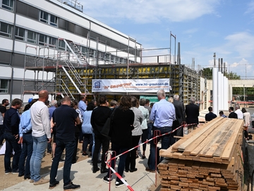 Besucherinnen und Besucher stehen vor der Baustelle und lauschen den Reden. Alle sind von hinten zu sehen.