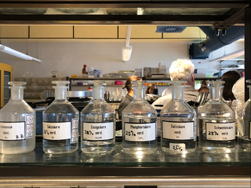 Eine Reihe mit Labor-Glasflaschen, gefüllt mit diversen Säuren in unterschiedlichen Verdünnungen.