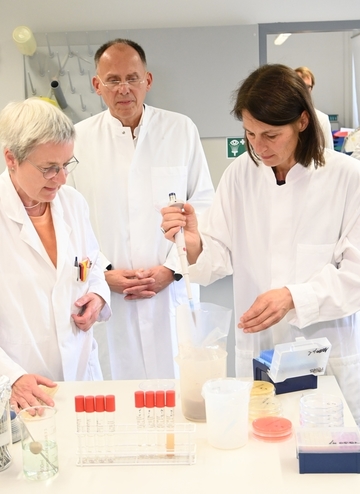 Ute Kuschfeldt, Prof. Dr. Eberhard Haunhorst und Ministerin Miriam Staudte stehen um einen Labortisch mit diversen Proben in Röhrchen herum.