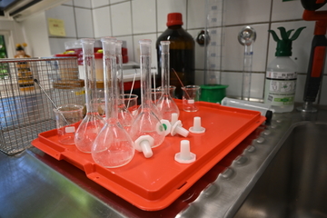 Bauchige Gläser mit langen Hälsen liegen auf einer orangen Platte neben dazugehörigen Plastikstopfen.