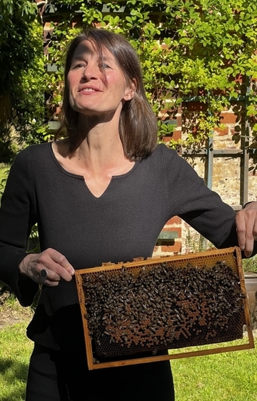 Ministerin Miriam Staudte hält einen Holzrahmen hoch. Darin befinden sich Waben auf denen Bienen sitzen.