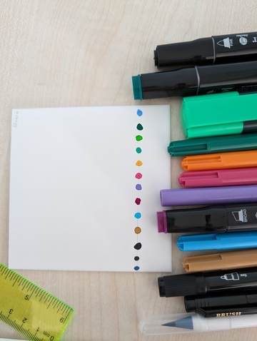 Filzstifte mit verschiedenen Farben liegen neben einem Blatt Papier. Mit den Filzstiften sind Punkte auf das Papier gemalt.