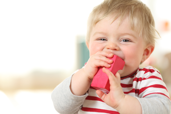 Ein Kleinkind steckt einen roten Bauklotz in den Mund.