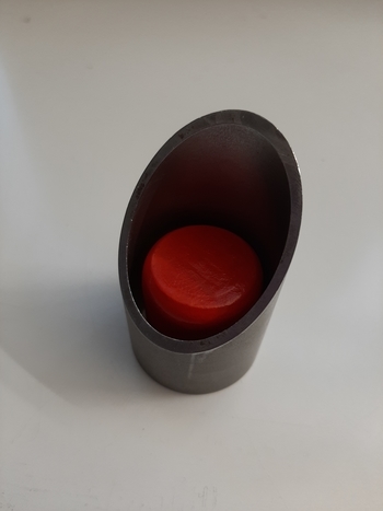 Zylinder zur Überprüfung, ob Spielzeug verschluckt werden kann. Der rote Holzklotz passt in den Zylinder rein und kann verschluckt werden.