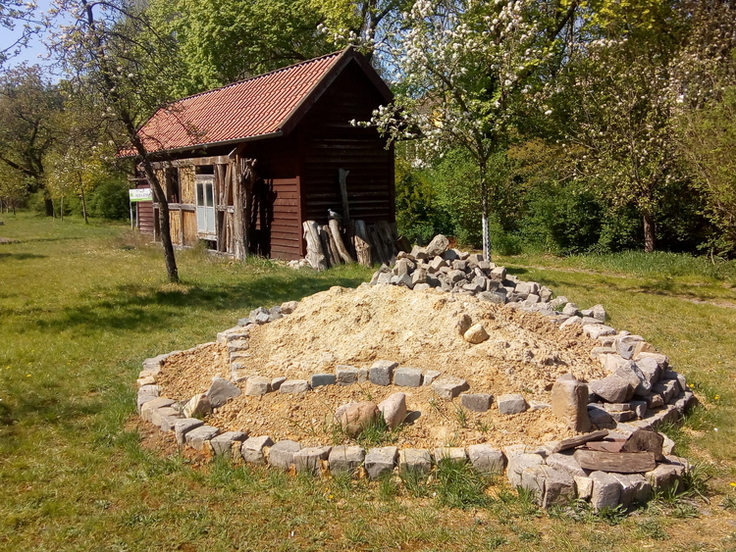 Ein Sandhügel, mit großen Feldsteinen abgegrenzt und wenigen Grasbüscheln bewachsten.