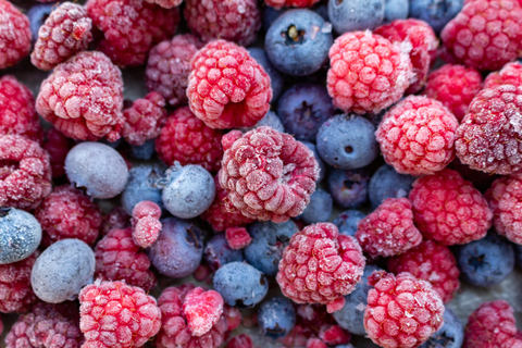 Gefrorene Himbeeren und Heidelbeeren liegen aufeinander und nebeneinander.