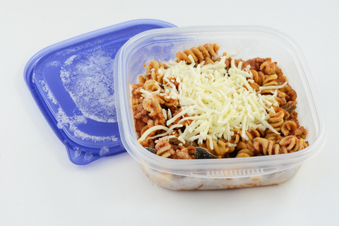Spaghetti Bolognese mit geriebenem Käse liegt gefroren in einem Plastikbehälter.