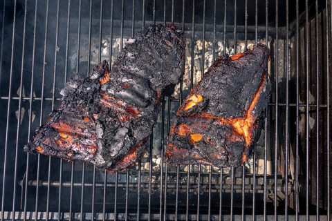 Zwei völlig verkohlte Stücke Fleisch liegen auf einem Grillrost.