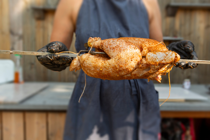 Ein rohes Grillhähnchen wurde mariniert und auf einen Grillspieß gesteckt.