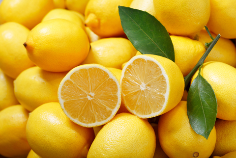 Eine aufgeschnittene Zitrone liegt auf mehreren ganzen Zitronen.