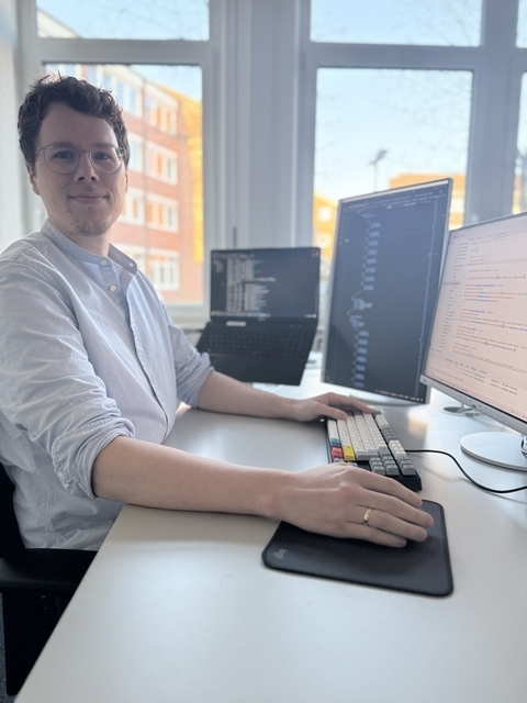 Der Ausbildungsleiter für den Ausbildungsberuf Fachinformatiker/-in Systemintegration an seinem Arbeitsplatz vor Bildschirmen mit Quellcode