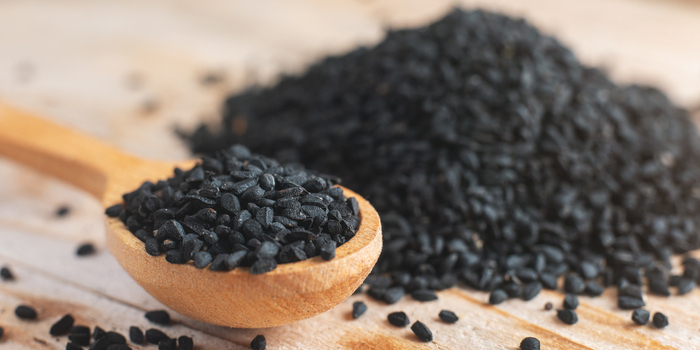 Schwarzkümmelsamen auf einem Holzlöffel vor Holzgrund