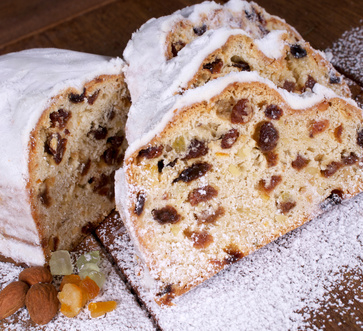 Weihnachtsstollen davon drei Scheiben aufgeschnitten auf dunklem Untergrund