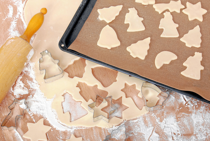 Ausgerollter Teig auf einer Holzoberfläche und ausgestochene Kekse auf einem Backblech