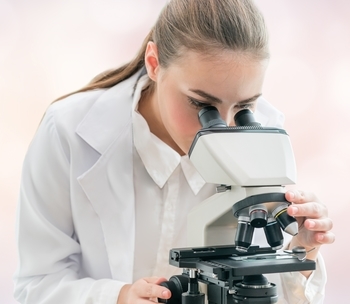 Eine Chemielaborantin blickt durch ein Mikroskop