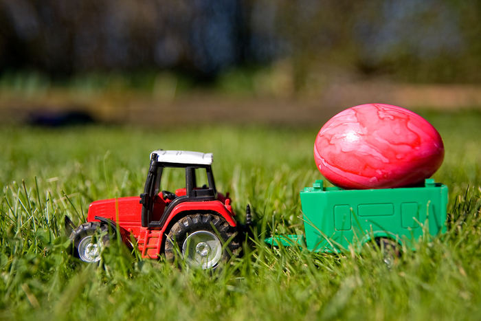 Spielzeugtrecker mit Anhänger und Osterei auf grünem Rasen