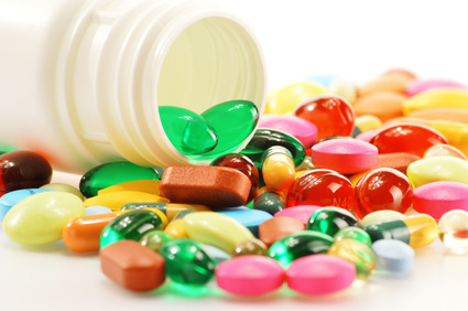 Neben einer geöffneten Tablettendose liegen viele bunten Kapseln und Tabletten.