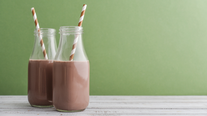 Zwei Flaschen Schokoladenmilch mit Trinkhalmen auf grünem Hintergrund.