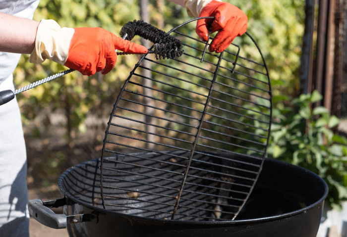 Mensch mit roten Handschuhen reinigt runden Grill mit Bürste