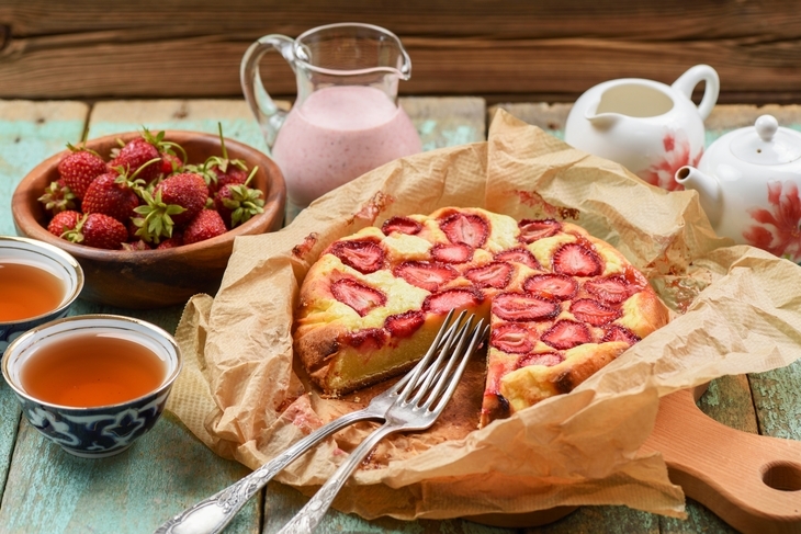 Erdbeerkuchen auf Backpapier, daneben zwei gefüllte Teetassen.