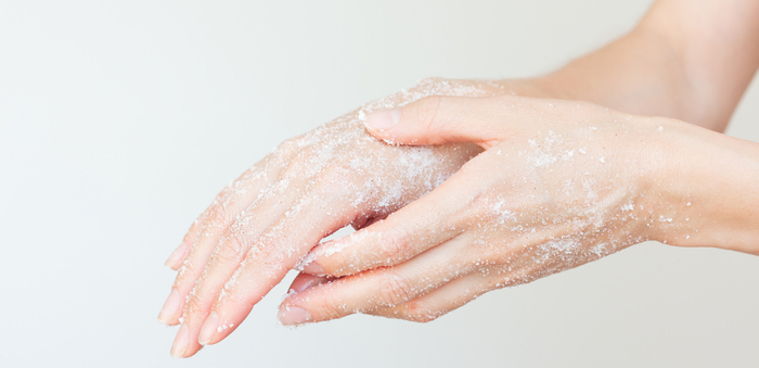 Frau die ein weißes Zuckerpeeling auf ihre Hand aufträgt