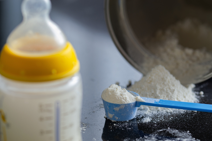 Gefüllte Babyflasche neben gehäuftem Löffel mit Milchpulver.